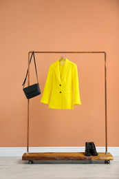 Photo of Rack with stylish women's clothes and boots near color wall