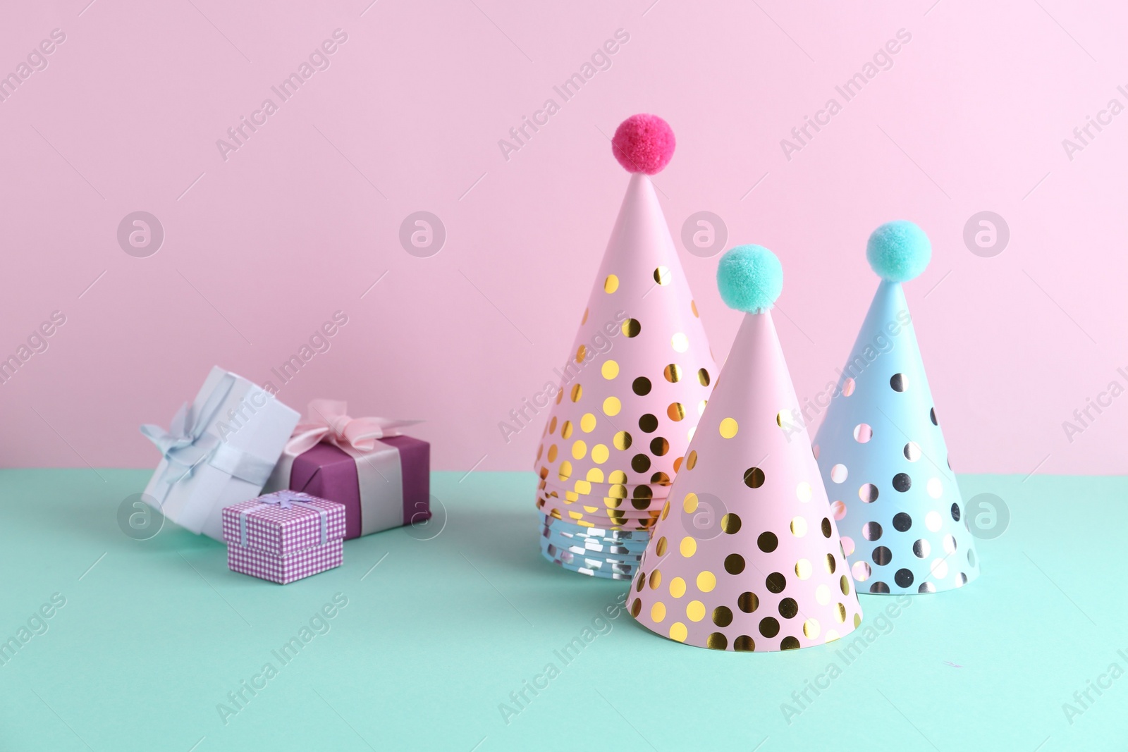 Photo of Party hats and gift boxes on color background