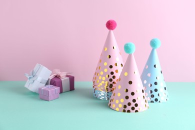 Party hats and gift boxes on color background