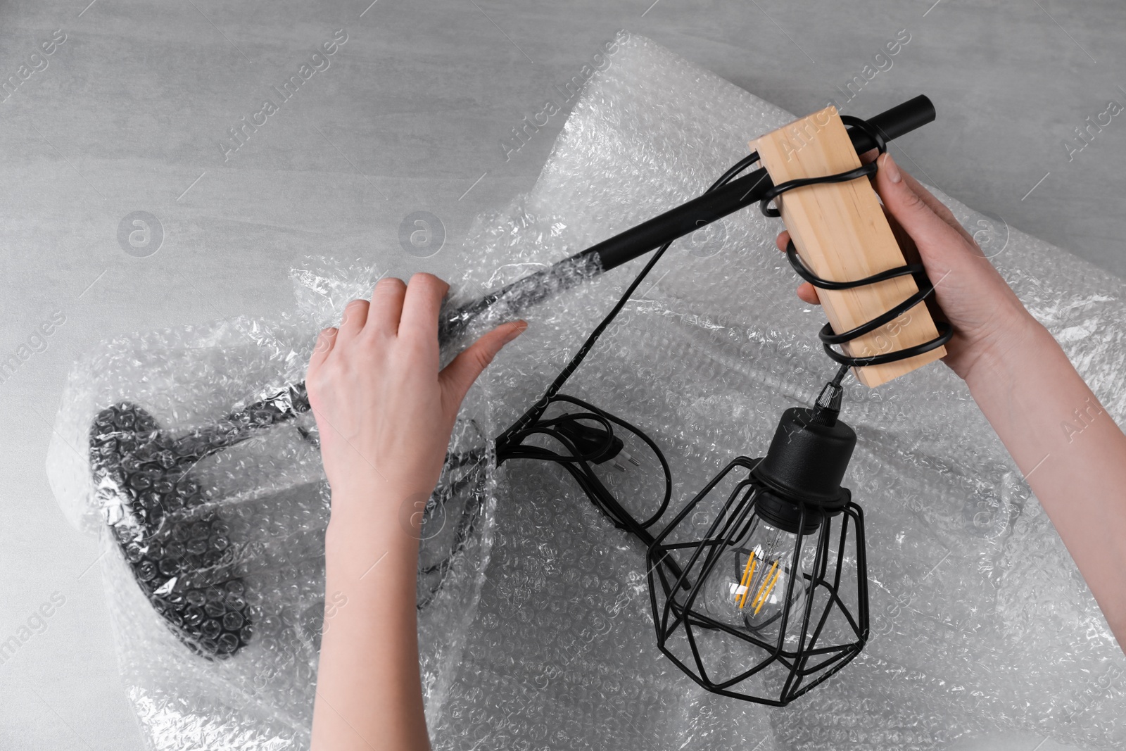 Photo of Woman covering lamp with bubble wrap at light grey table, closeup