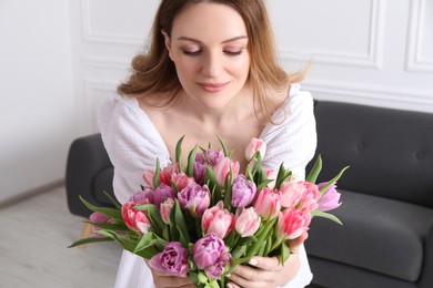 Photo of Young woman with bouquet of beautiful tulips indoors