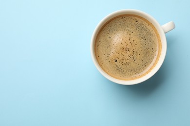 Aromatic coffee in cup on light blue background, top view. Space for text