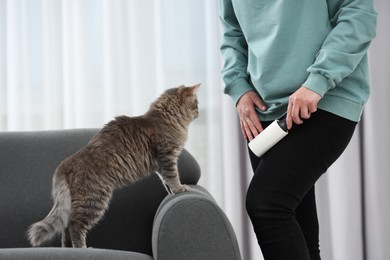 Photo of Pet shedding. Woman with lint roller removing cat`s hair from trousers at home, closeup