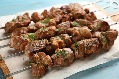 Photo of Metal skewers with delicious meat served on light blue wooden table, closeup