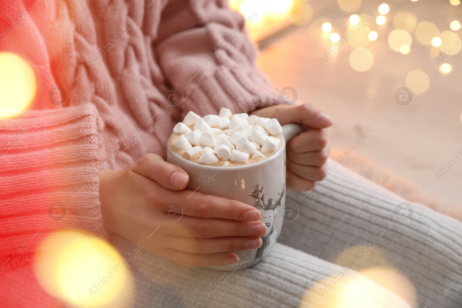 Photo of Woman holding cup of hot drink with marshmallows indoors, closeup. Magic Christmas atmosphere