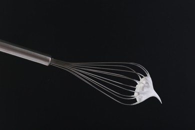Photo of Whisk with whipped cream on black background