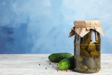 Photo of Jar with pickled cucumbers on white wooden table against blue background, space for text