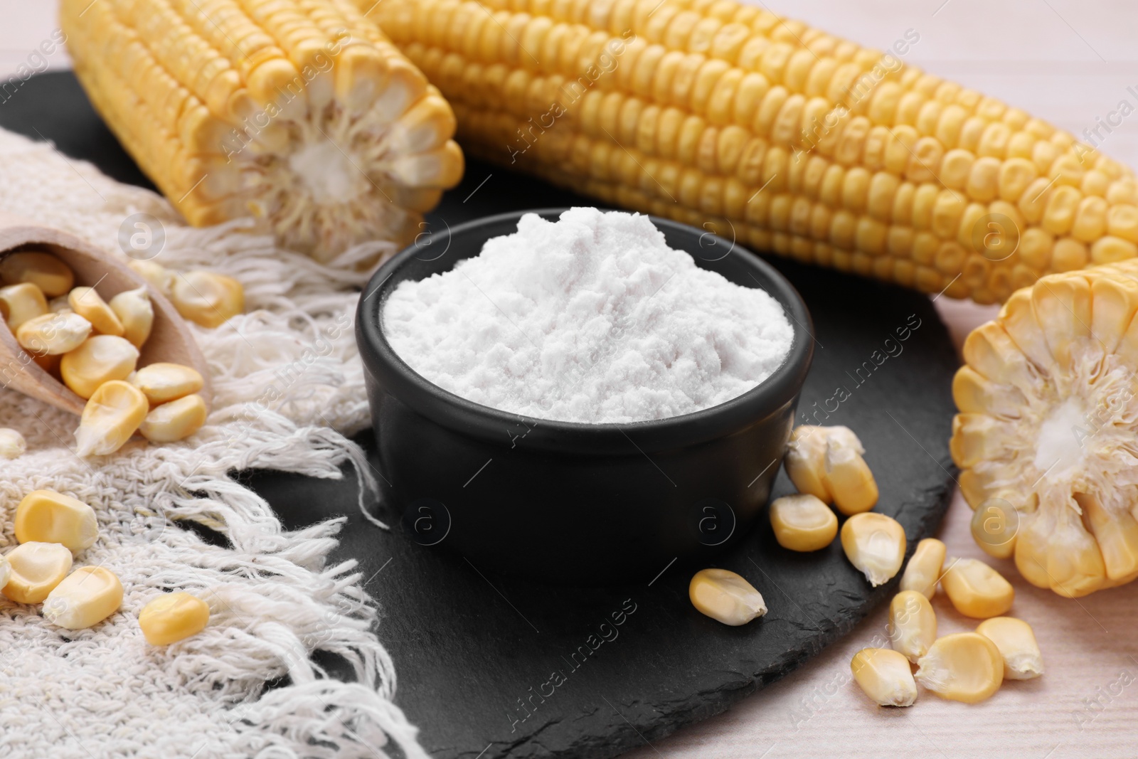 Photo of Bowl with corn starch, ripe cobs and kernels on wooden table