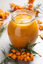 Photo of Delicious sea buckthorn jam and fresh berries on grey table