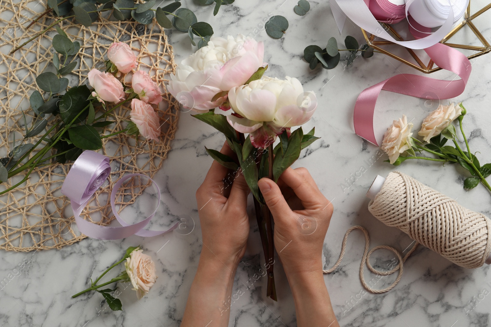 Photo of Florist creating beautiful bouquet at white marble table, top view