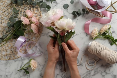 Florist creating beautiful bouquet at white marble table, top view