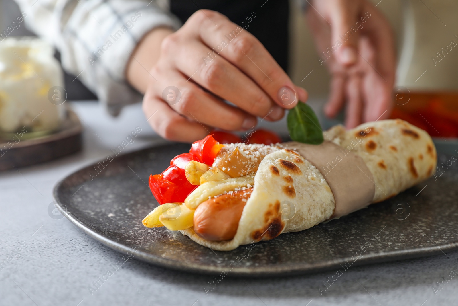 Photo of Woman cooking delicious pita wrap with sausage, french fries and pepper at light gray table, closeup