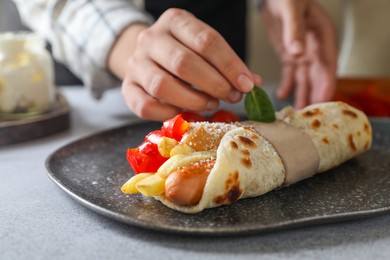 Woman cooking delicious pita wrap with sausage, french fries and pepper at light gray table, closeup