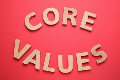 Photo of Phrase CORE VALUES made of wooden letters on red background, flat lay