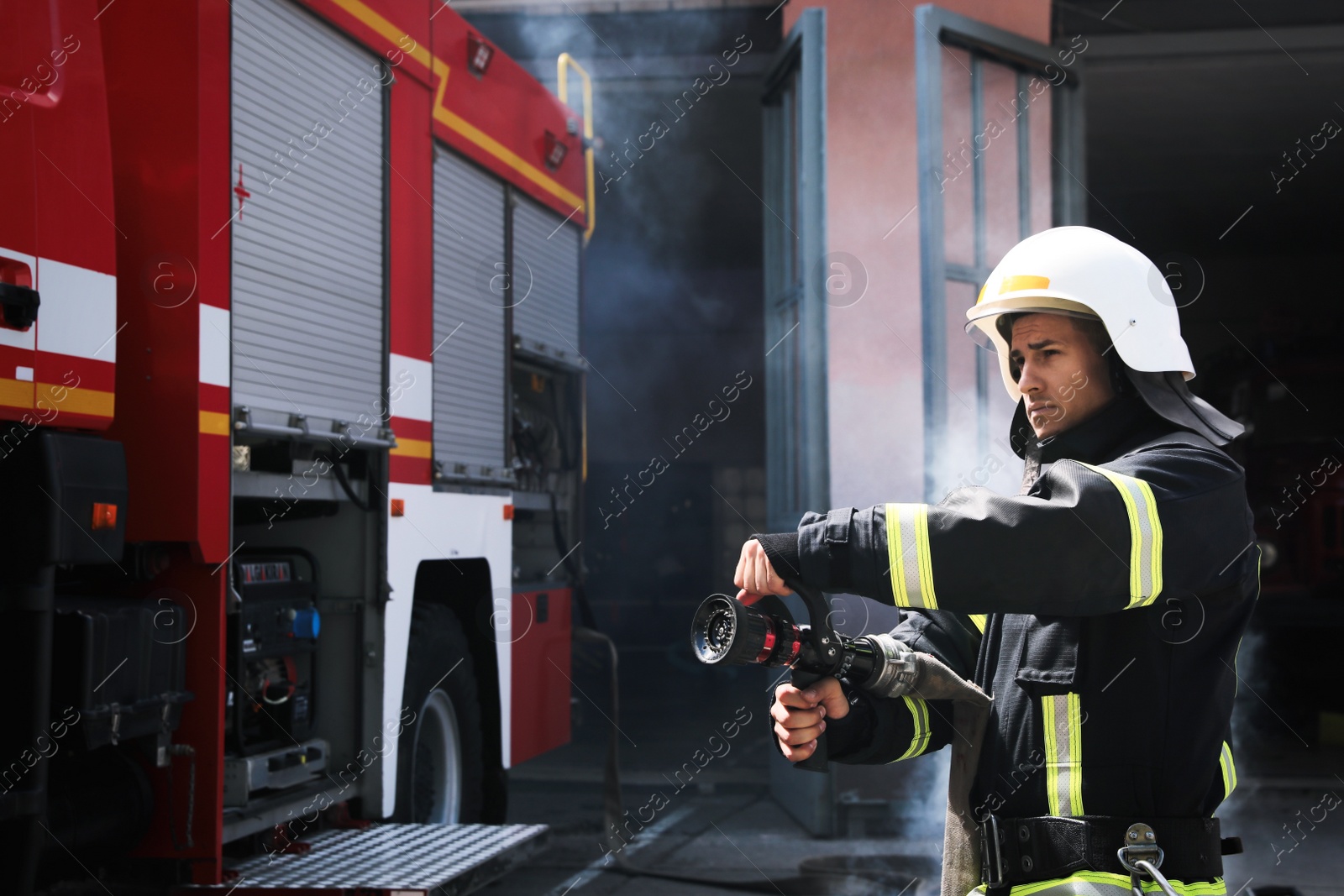 Photo of Firefighter in uniform with high pressure water jet near fire truck outdoors