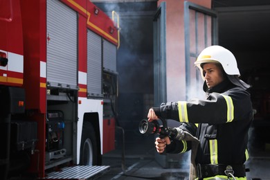 Firefighter in uniform with high pressure water jet near fire truck outdoors