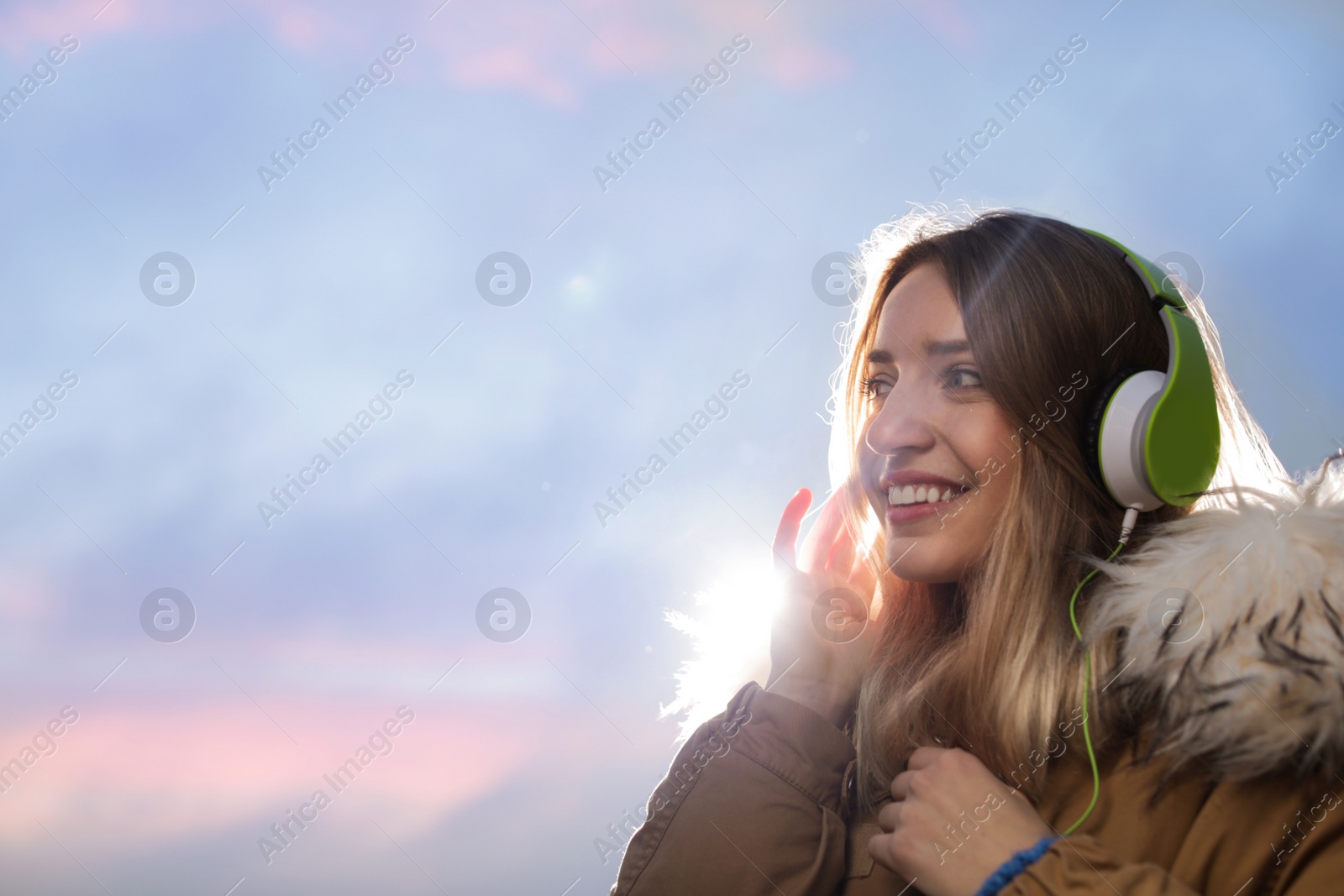 Photo of Young woman with headphones listening to music outdoors, space for text