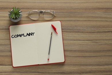 Image of Notebook with word Complaint, eyeglasses and houseplant on wooden table, flat lay. Space for text