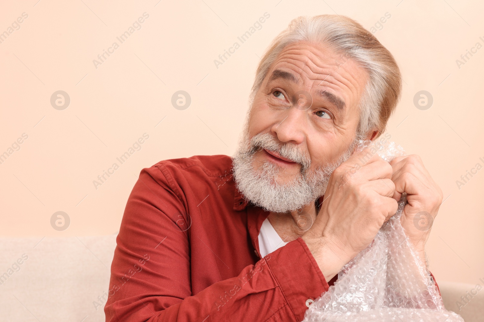 Photo of Senior man popping bubble wrap at home, space for text. Stress relief