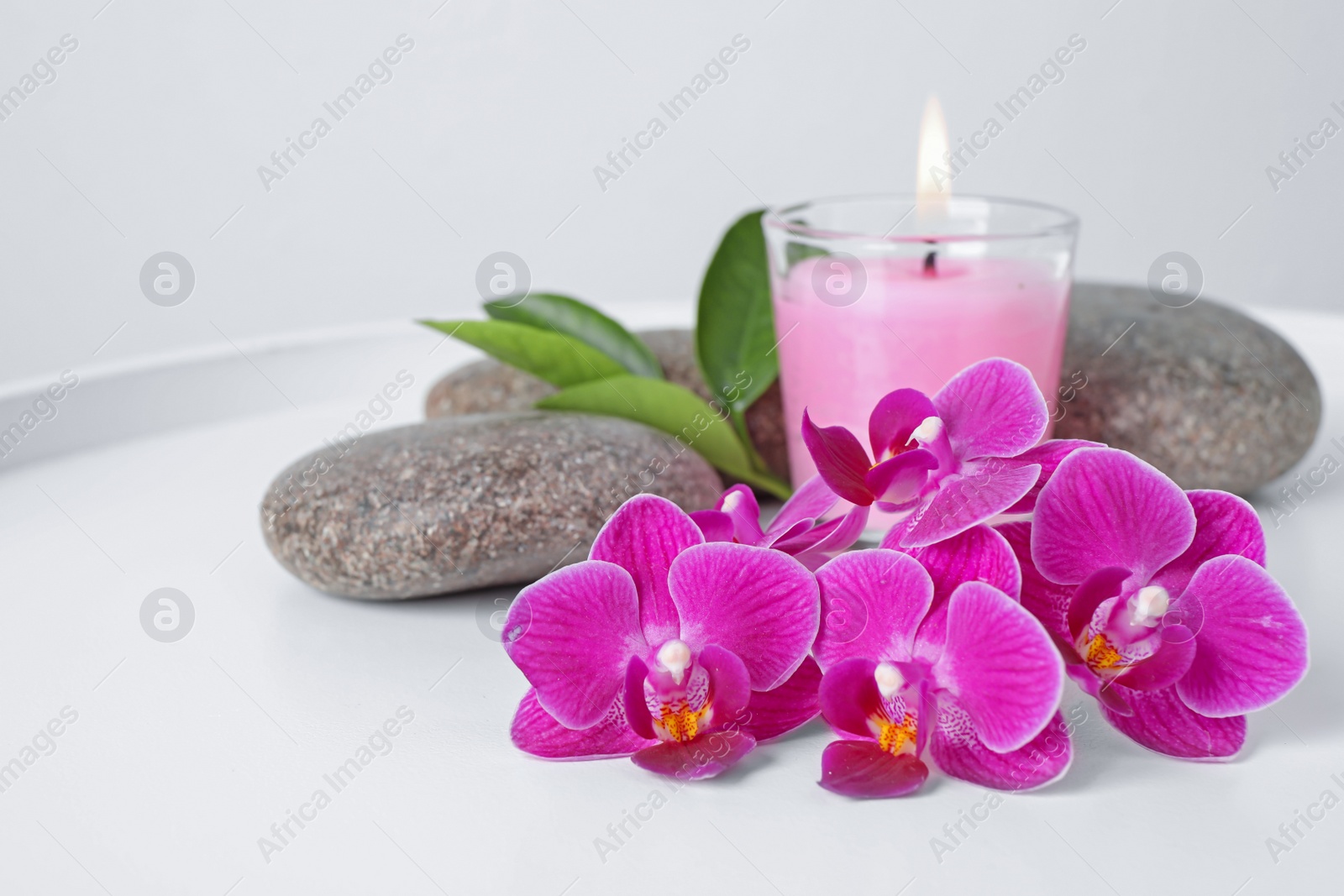 Photo of Spa stones, orchid flowers and candle on white table