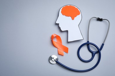 Photo of Human head cutout, brain, orange ribbon and stethoscope on grey background, flat lay with space for text. Multiple sclerosis concept