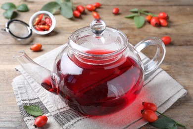 Teapot with aromatic rose hip tea and fresh berries on wooden table