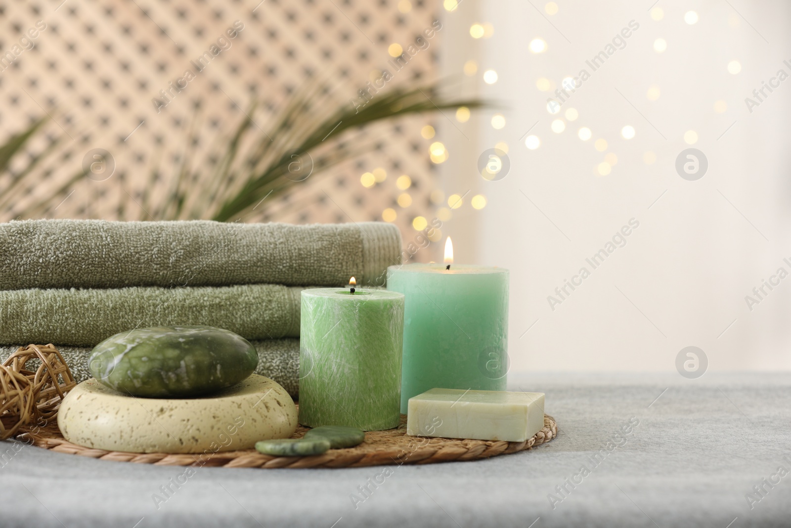 Photo of Spa composition. Burning candles, stones, soap and towels on soft grey surface, space for text