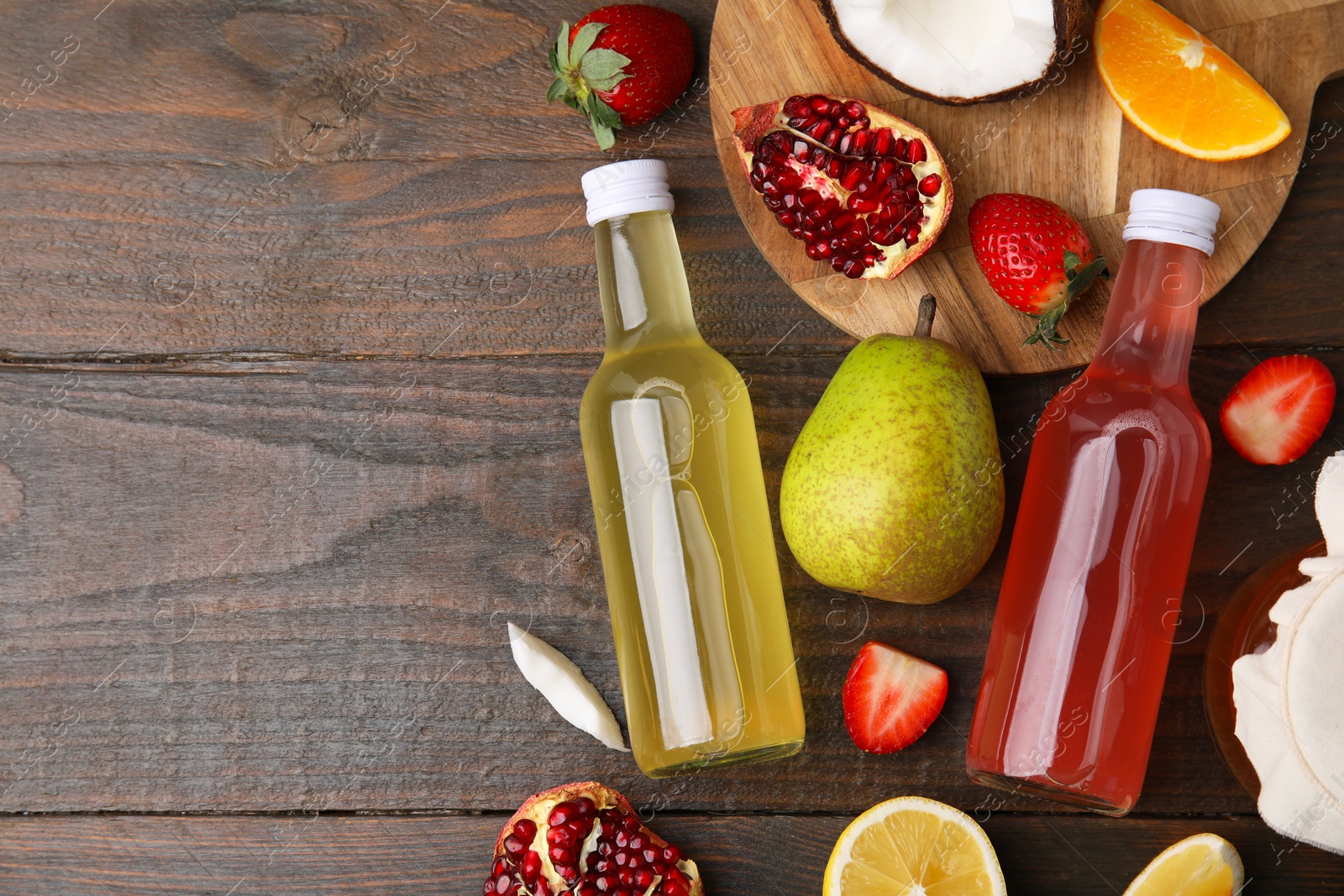 Photo of Delicious kombucha in glass bottles, fresh fruits and coconut on wooden table, flat lay. Space for text