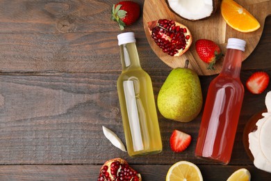 Delicious kombucha in glass bottles, fresh fruits and coconut on wooden table, flat lay. Space for text