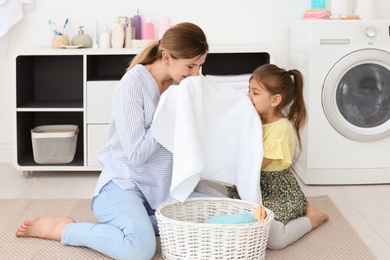 Housewife with daughter folding freshly washed towels in laundry room