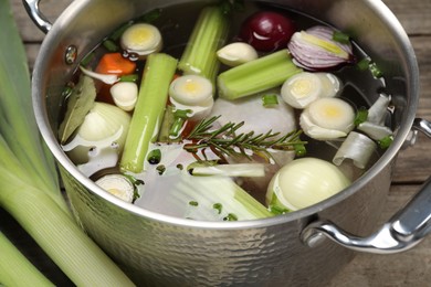 Photo of Different ingredients for cooking tasty bouillon in pot and celery on wooden table, closeup