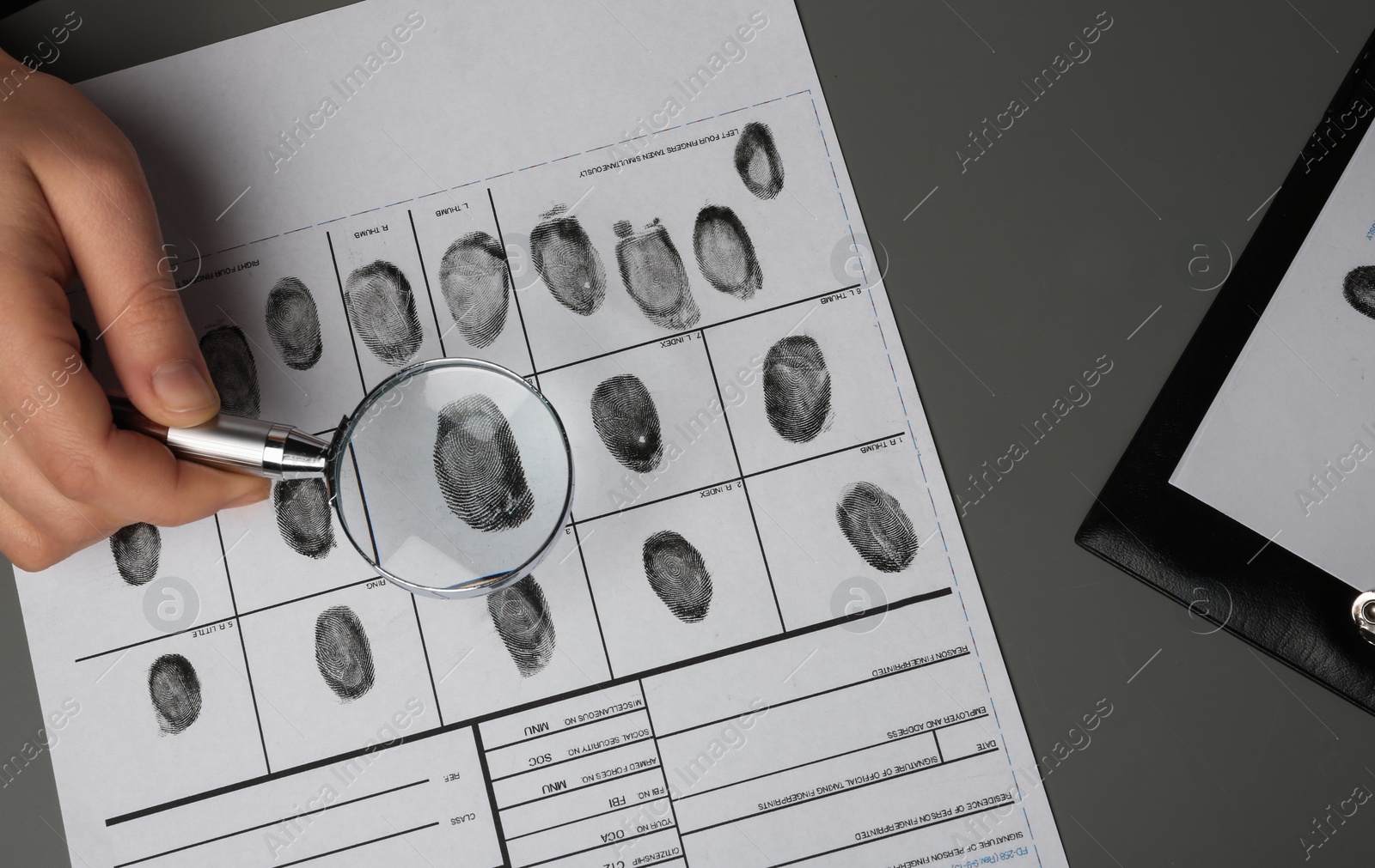 Photo of Criminalist studying fingerprints with magnifying glass, top view