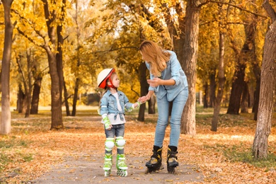 Mother and her daughter roller skating in autumn park