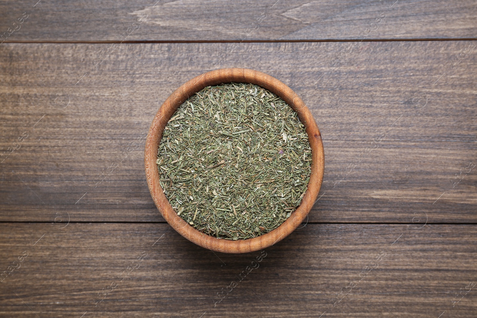Photo of Bowl of dried dill on wooden table, top view