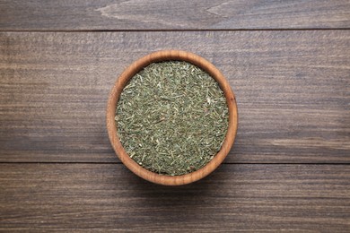 Photo of Bowl of dried dill on wooden table, top view