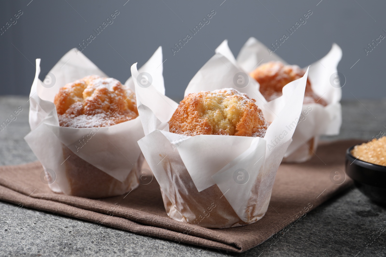 Photo of Delicious muffins with powdered sugar on grey table, closeup