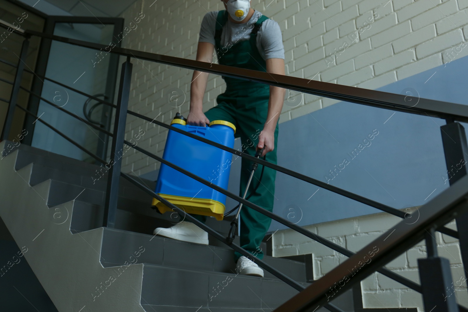 Photo of Pest control worker spraying pesticide on stairs indoors, closeup