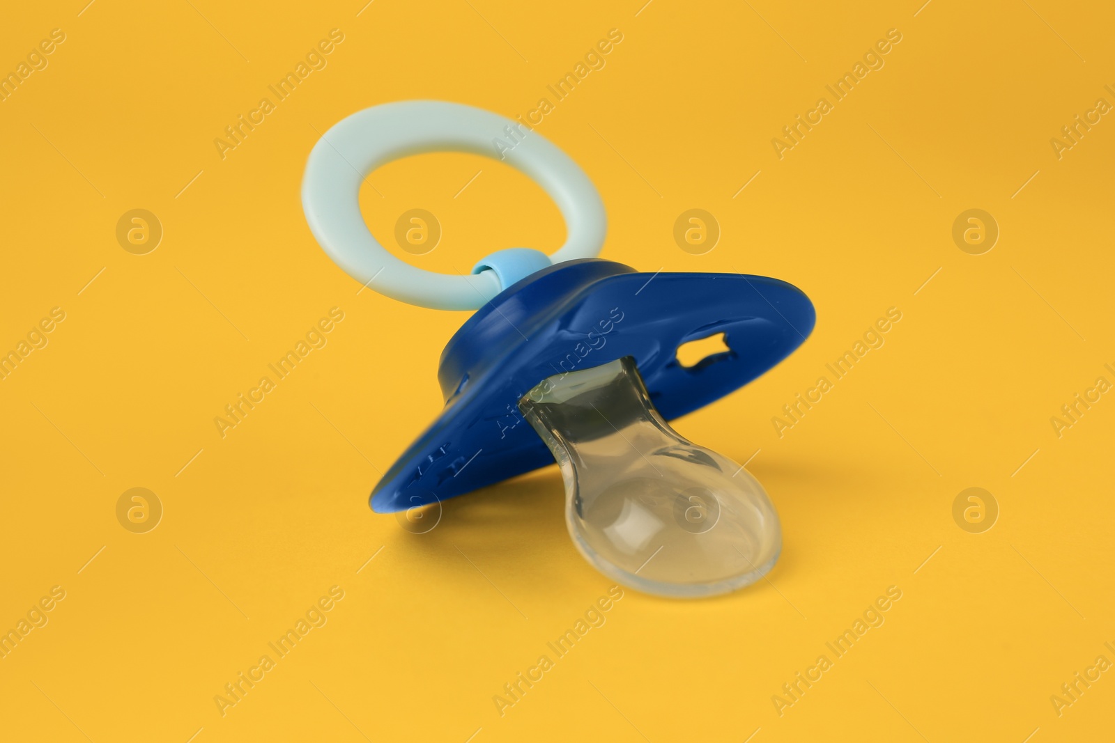 Photo of One blue baby pacifier on orange background, closeup