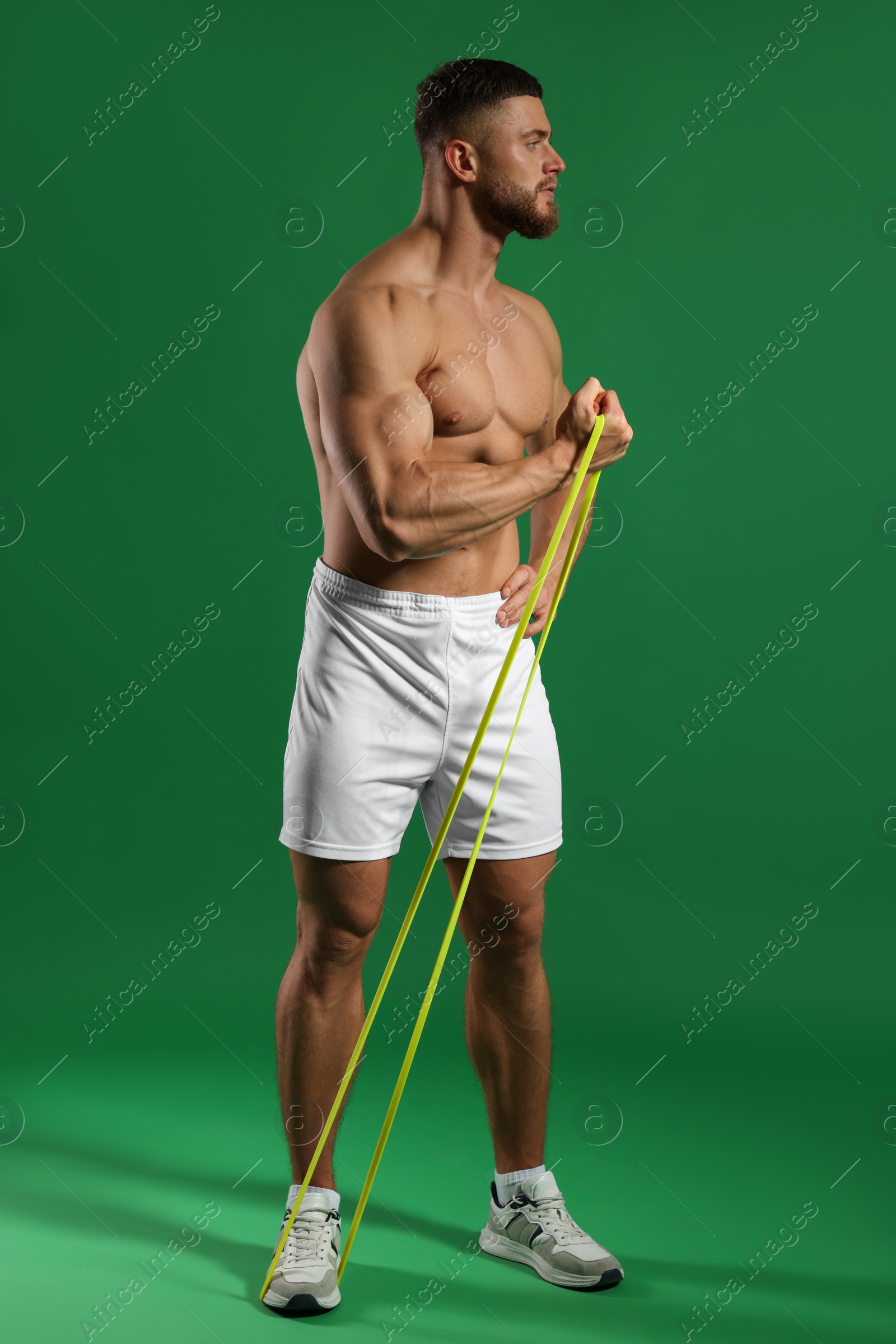 Photo of Muscular man exercising with elastic resistance band on green background