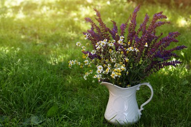 Photo of Beautiful bouquet with field flowers in jug on green grass. Space for text
