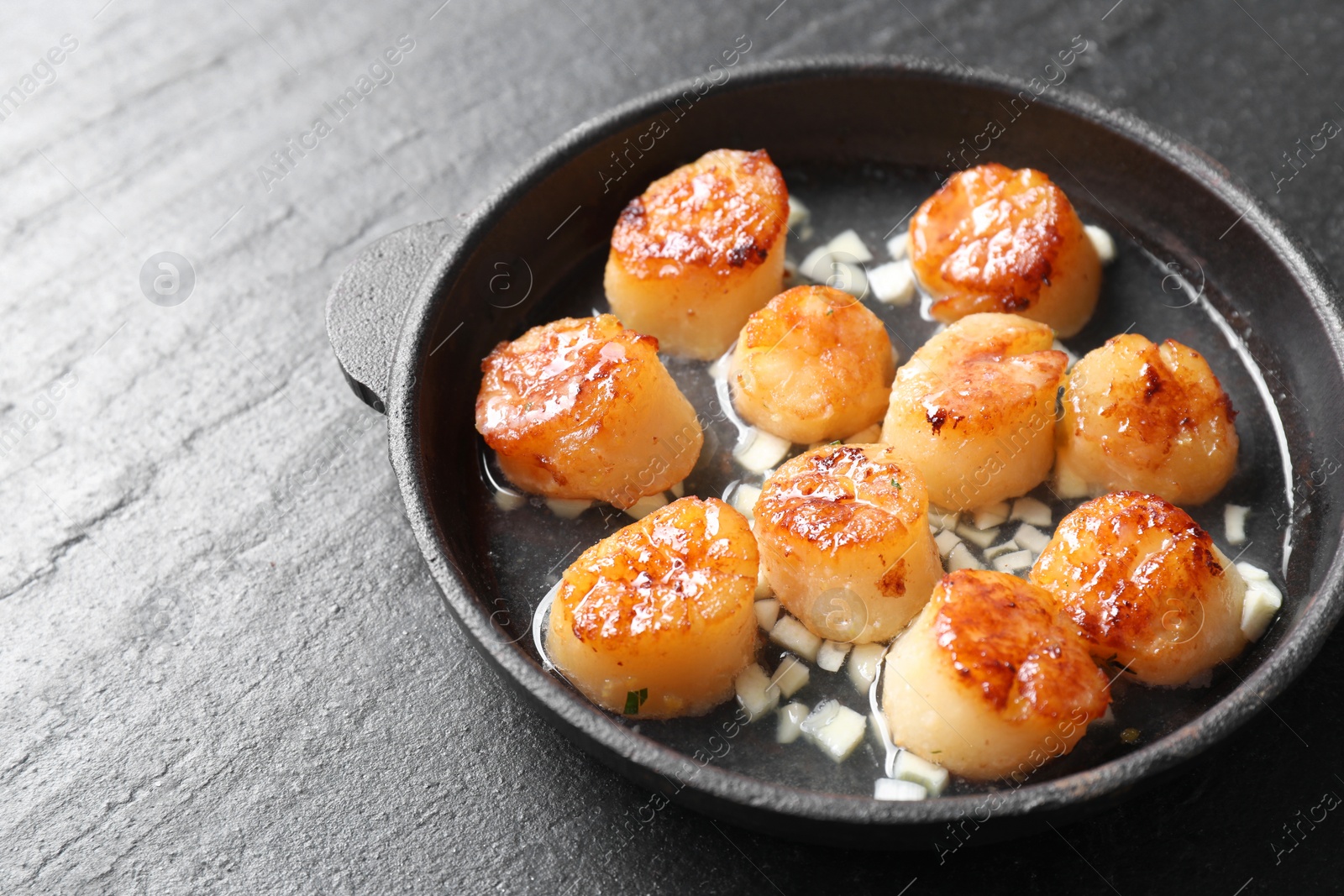 Photo of Delicious fried scallops in dish on dark gray textured table, closeup