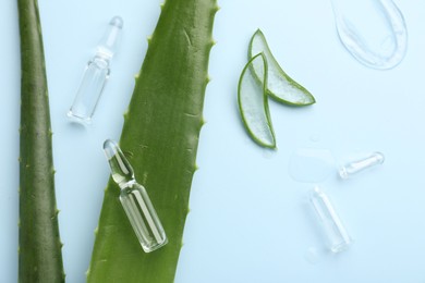 Flat lay composition with skincare ampoules and aloe leaves on light blue background