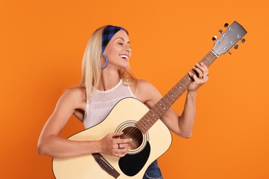 Photo of Happy hippie woman playing guitar on orange background