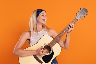 Happy hippie woman playing guitar on orange background