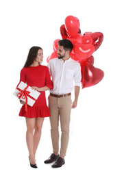 Photo of Happy young couple with gift box and heart shaped balloons isolated on white. Valentine's day celebration