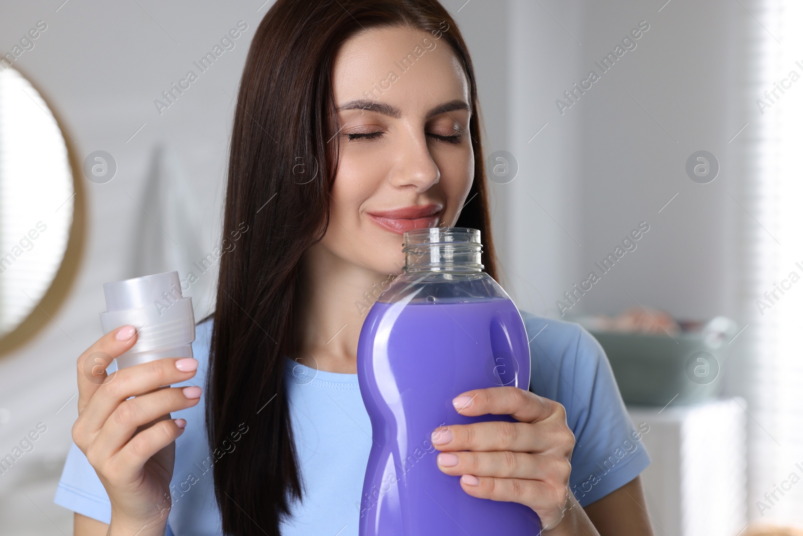 Photo of Woman smelling fabric softener in bathroom, space for text