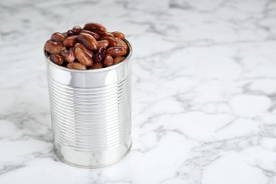 Photo of Tin can with kidney beans on white marble table, space for text