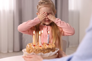 Birthday celebration. Mother holding tasty cake with burning candles near her daughter indoors