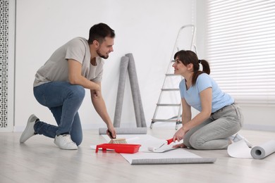 Couple applying glue onto wallpaper sheet in room