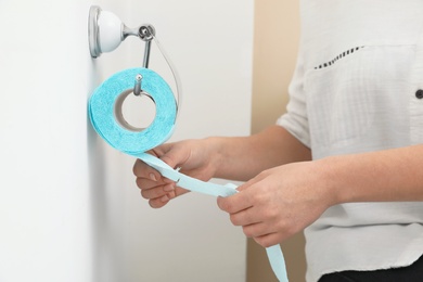 Woman taking toilet paper from roll holder in bathroom, closeup